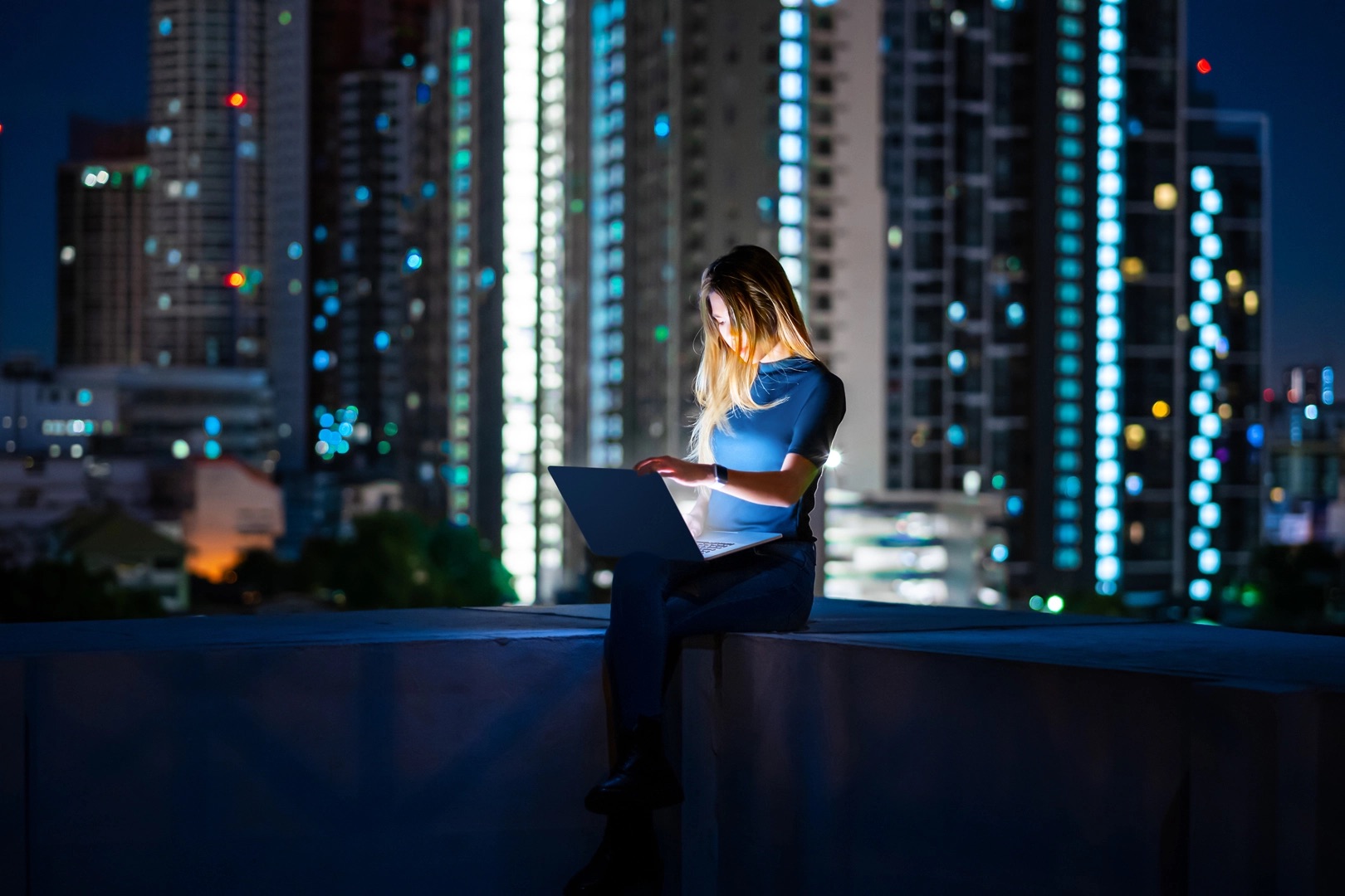 Woman using laptop on the rooftop of building for freelance work during night .